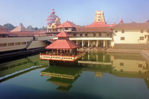 Holy Shrine dedicated to Hindu Deity, Lord Krishna. Picture taken in the town of Udupi, in the state of Karnataka, South India.   Picture shot on Feb 10, 2014, and shows the holy tank in the foreground, with the Temple towers seen in the background.  The building in the center of the tank, known as Mandapam, is where the sacred rituals are carried out. Four pillared corridors surround the tank with steps descending to the water.  This is for the convenience of devotees to take a dip in the holy tank, before entering the Temple. The holy tank here is named Madhava Sarovar, after the local saint Madhavacharya, who preached a form of Hinduism, several centuries ago.